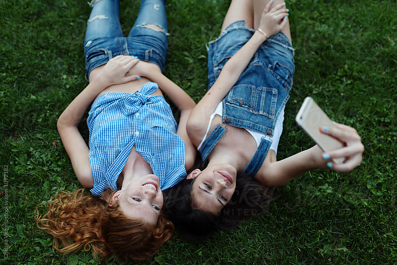 Two best friends laying in the grass taking pictures with their phone