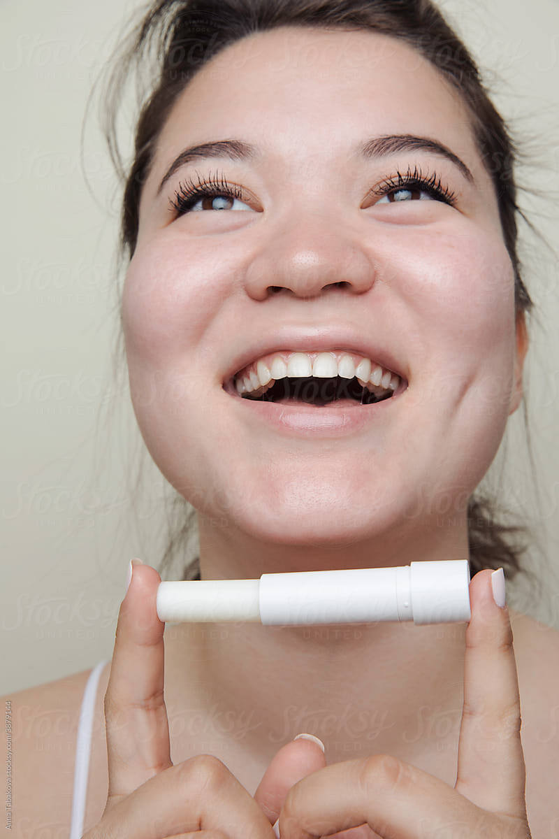 Eastern asian woman holding a lip balm laughing