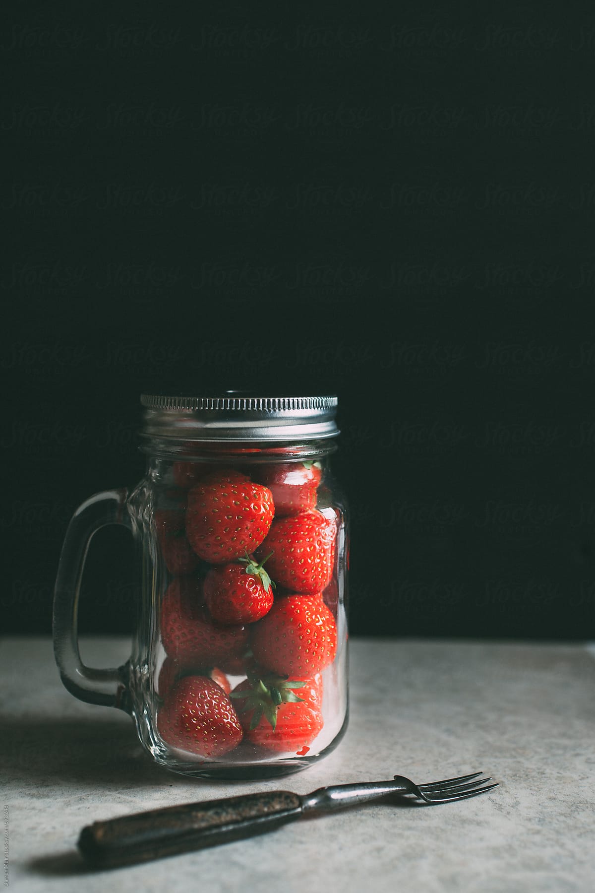 A jar of strawberries and a fork.