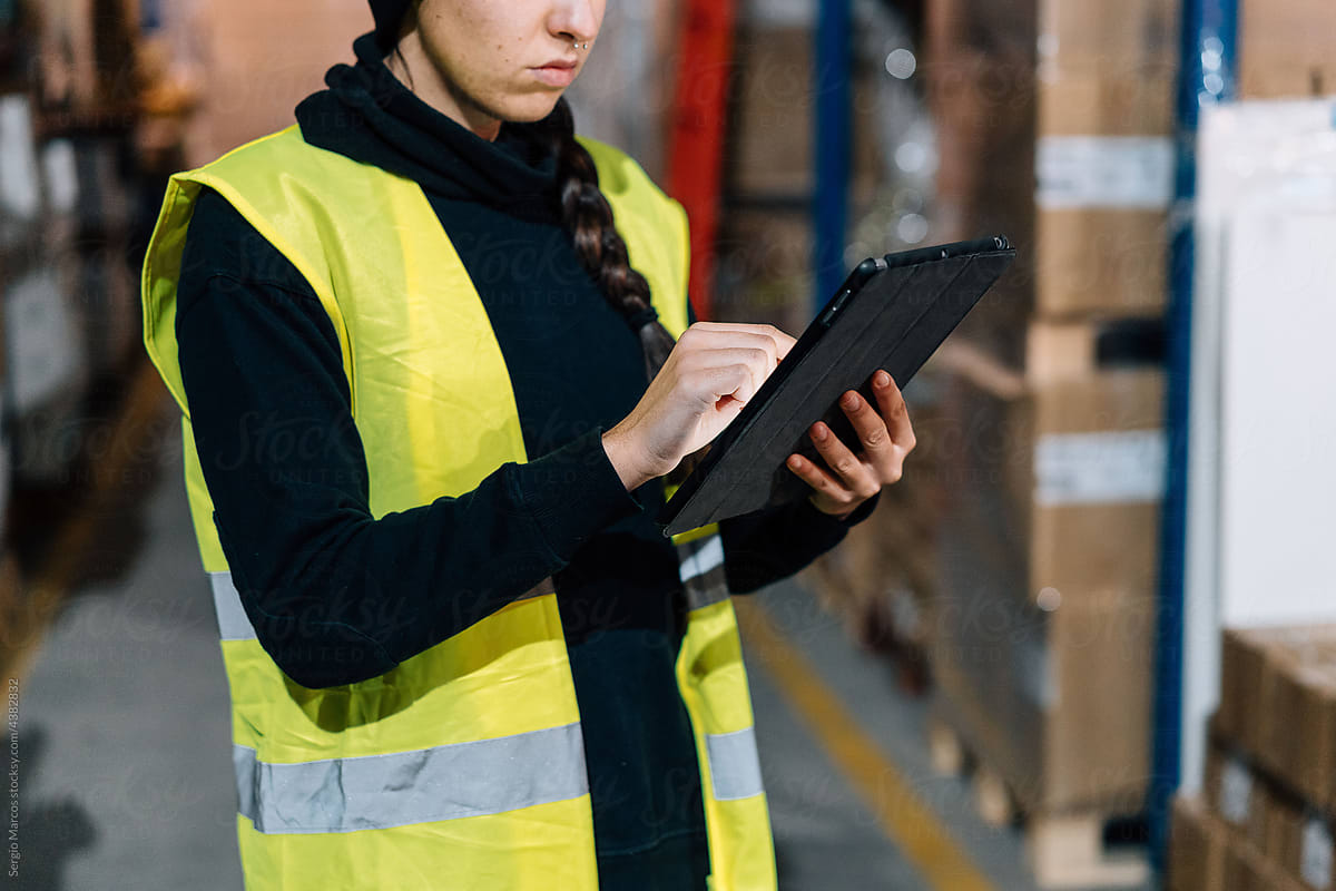 Crop Serious female worker using tablet in warehouse