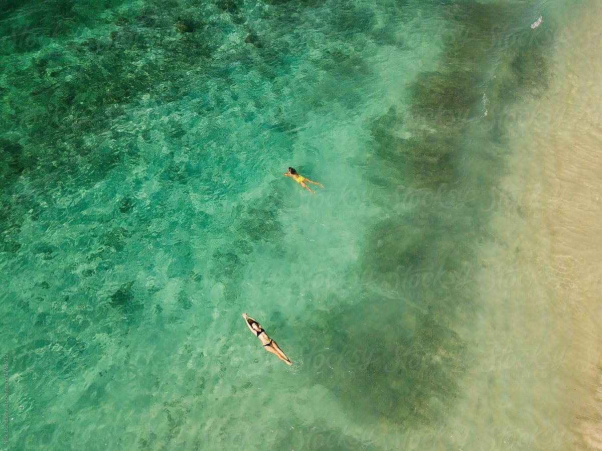 two persons, couple swimming together in the clear green ocean view from above,