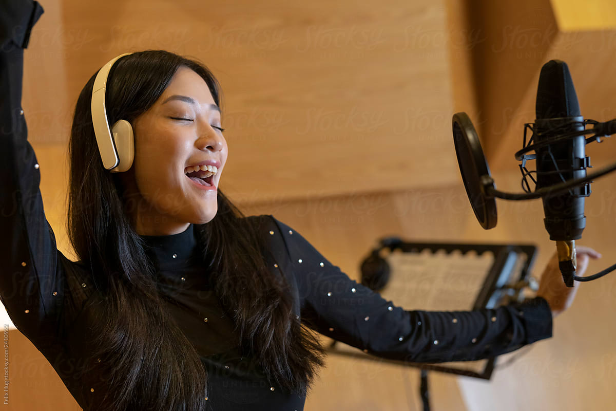 A close up of a woman singing in a recording studio, while having the headphones on.
