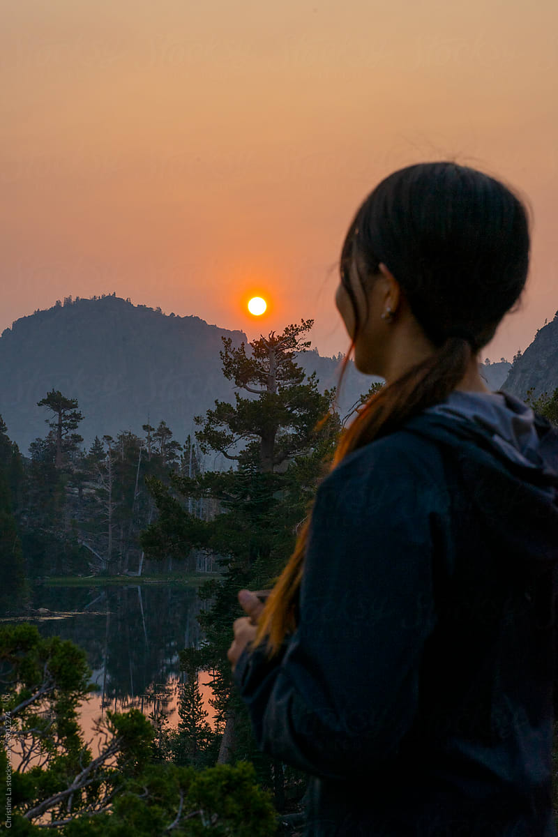 Woman looking at forest fire smoke and sunrise