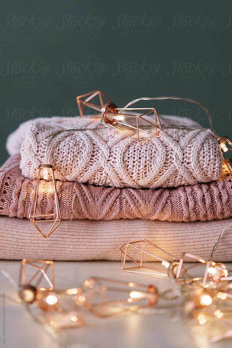 A stack of knitted sweaters with fairy lights garland..