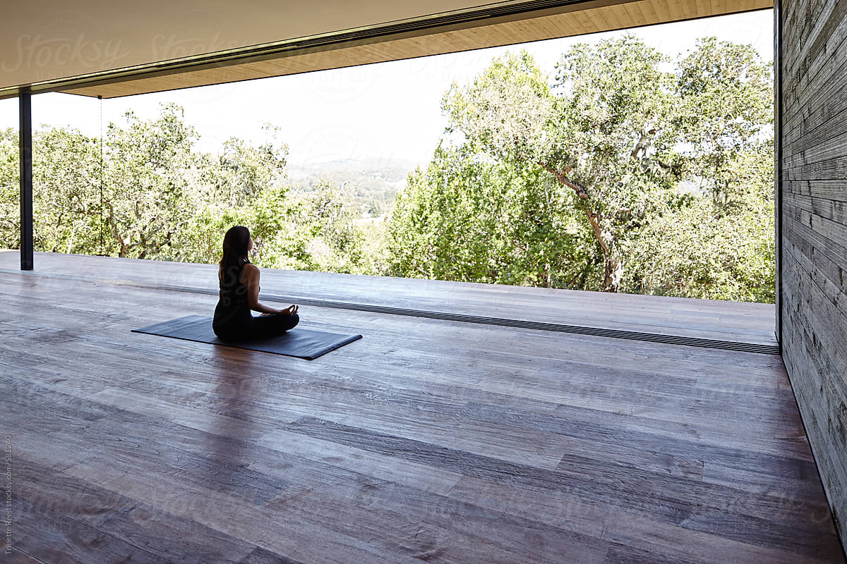 Woman meditating on yoga deck in modern design home
