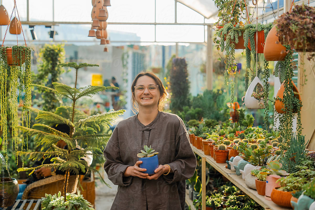 Woman standing in the greenhouse holding a plant