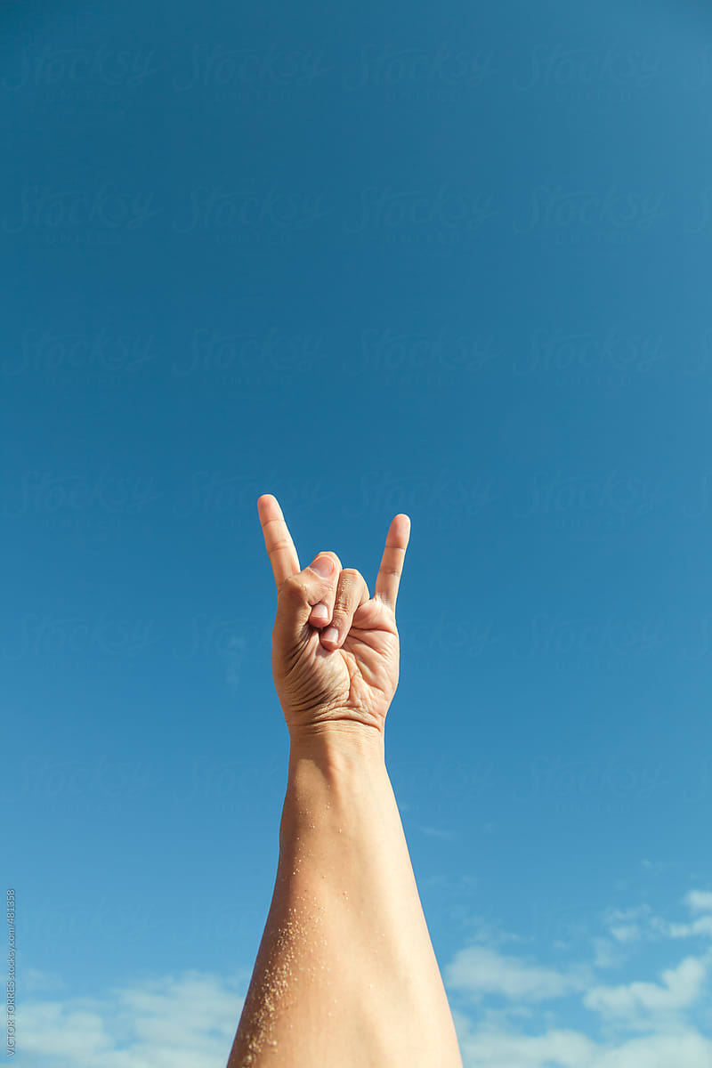 Person Making the Rock Hand Sign Against a Radiant Blue Sky