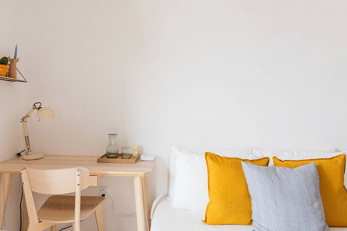 Yellow and white pillows on a bed next to a work station with a desk