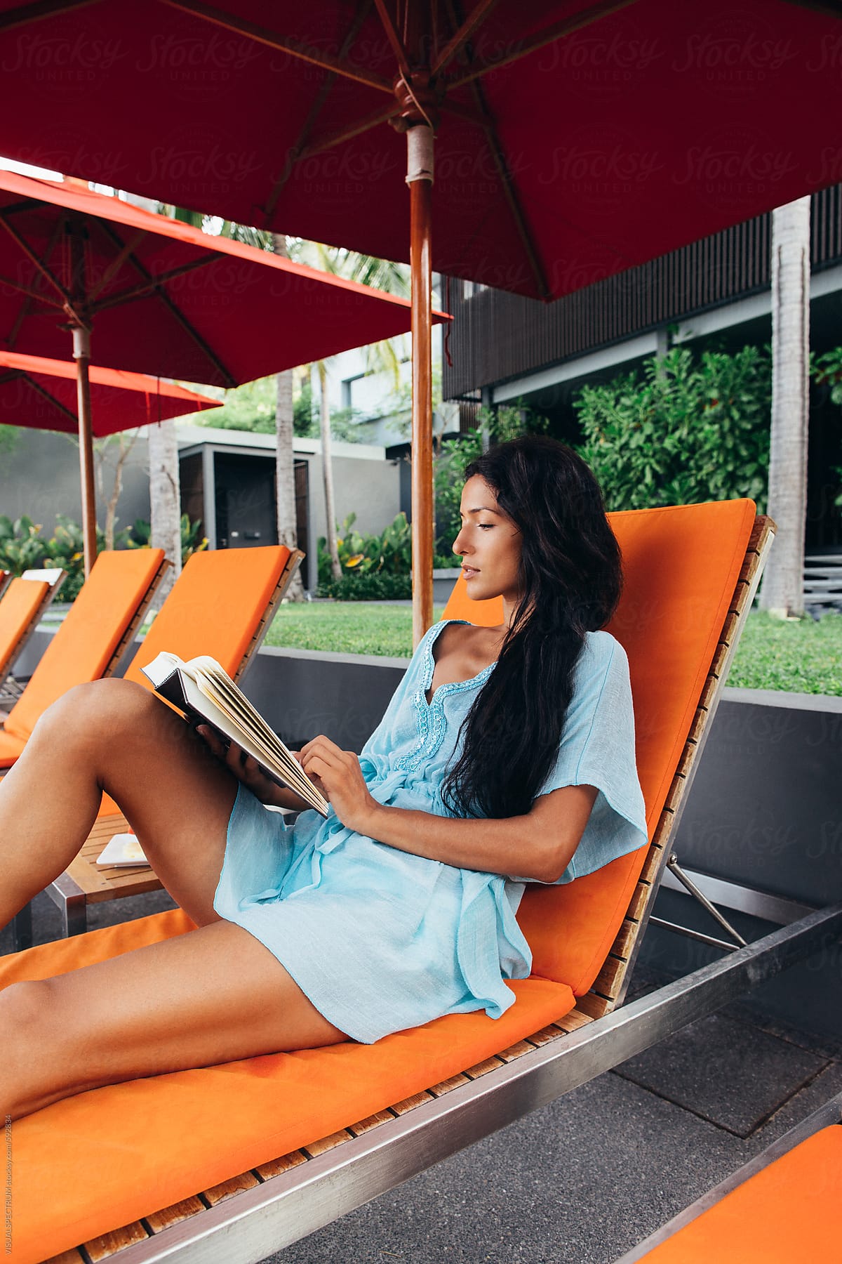 Pretty Long-Haired Woman Reading Book on Orange Sunbed