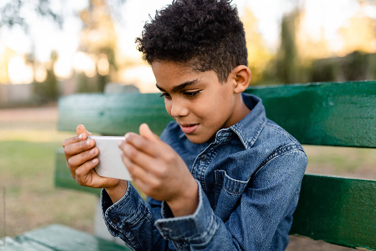 Young Boy Watches a Video on His Phone at the Park