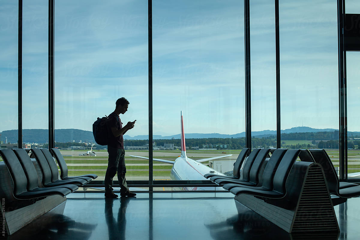 passenger using phone in airport, silhouette of man waiting for departure