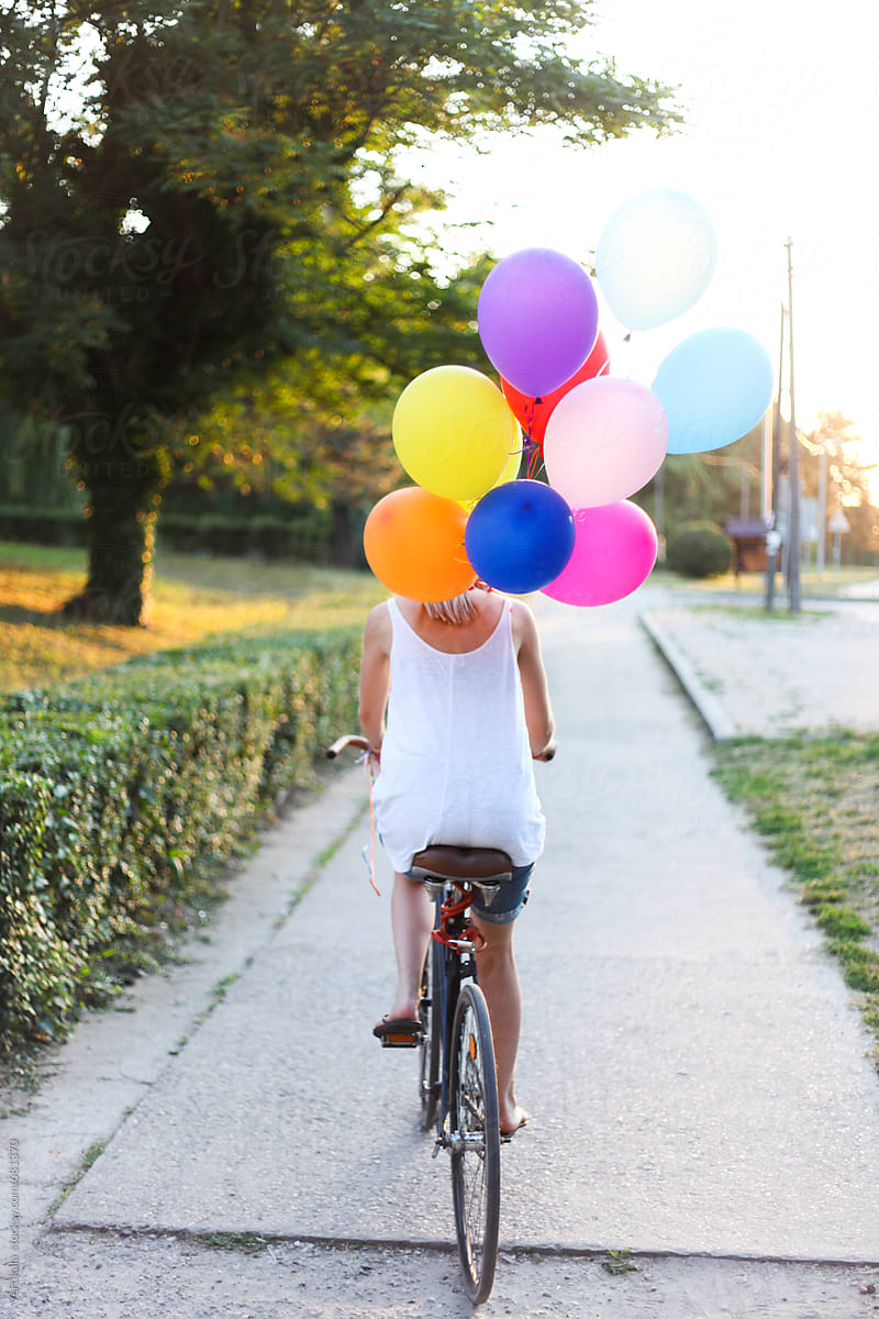 Woman riding a bicycle holding colorful ballons