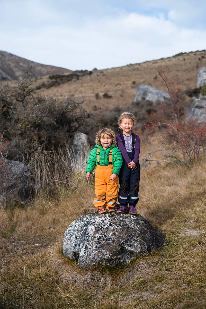Boy and girl stand on a limestone boulder, smiling for the camera, Castle Hill, New Zealand.