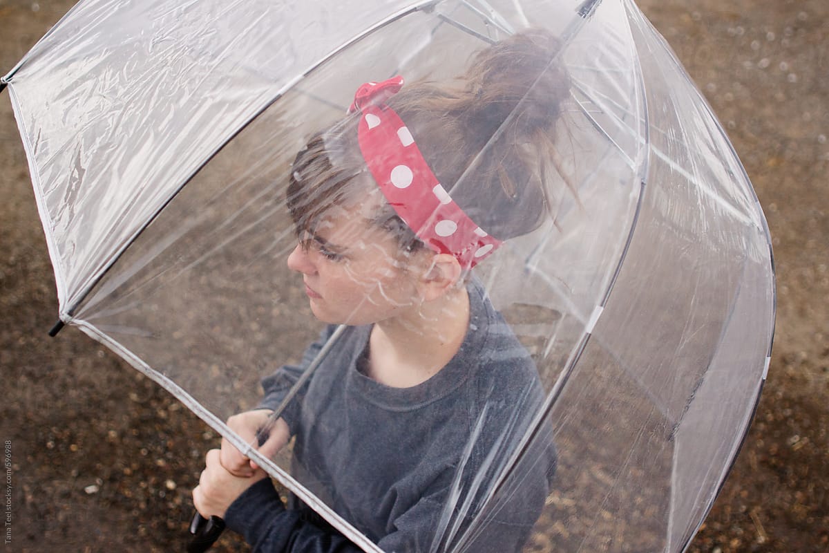 Teenager stands under clear umbrella