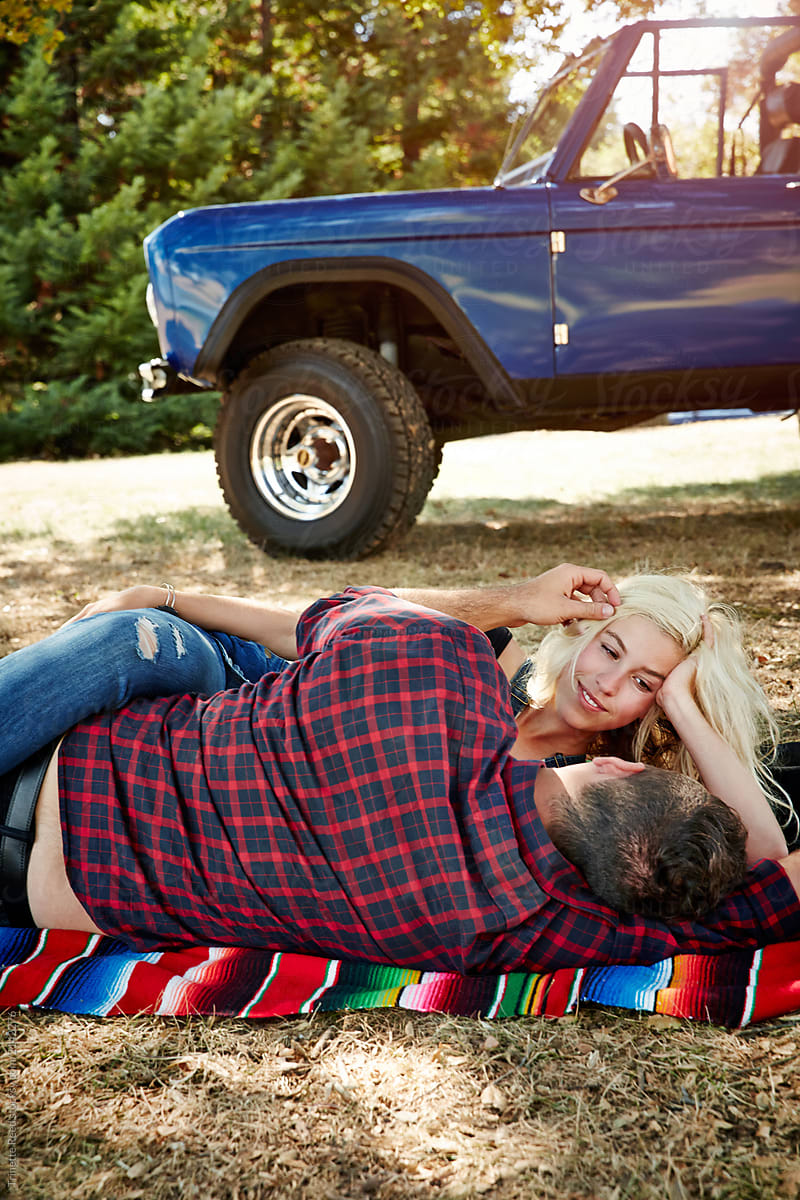 Millennial couple having a romantic moment lying on blanket in park while on road trip
