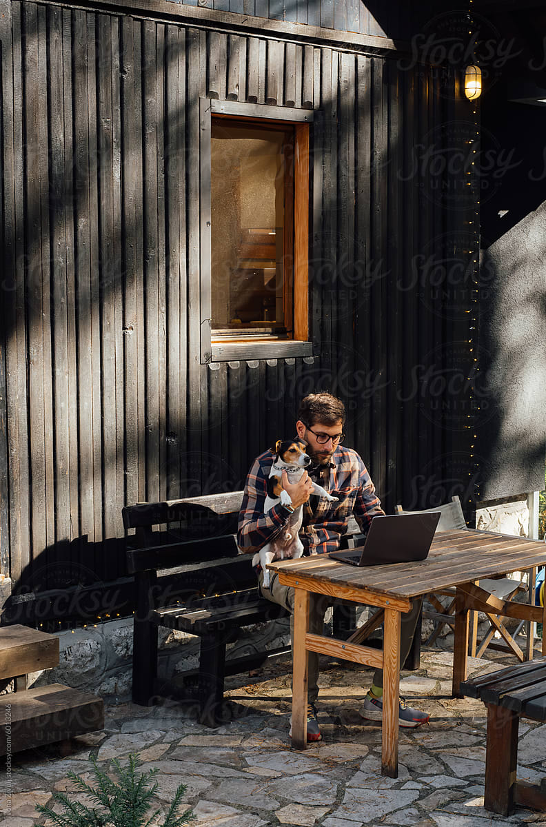 Man Holding His Dog While Remotely Working From His Mountain Cabin