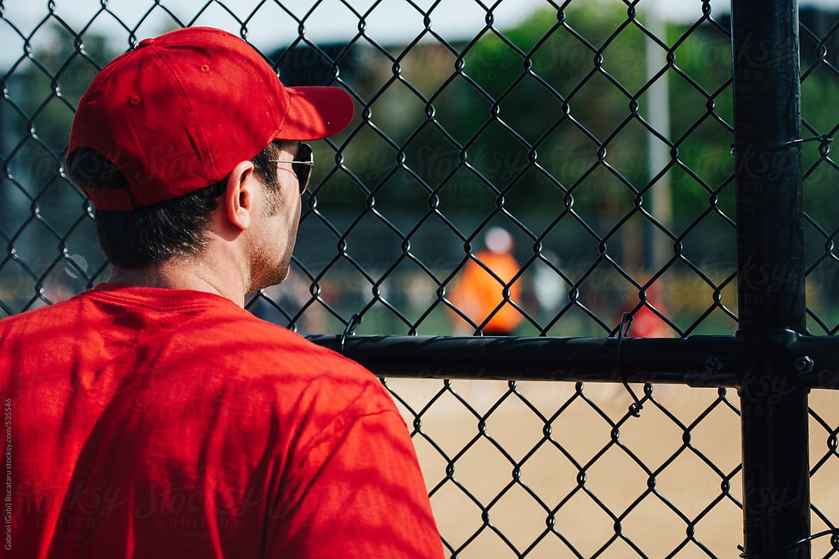 Baseball coach with red shirt and cap watching a game