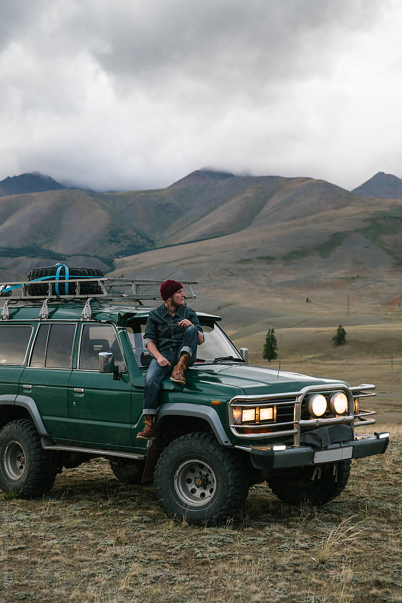 Young man sitting on the old green jeep parked in wild area