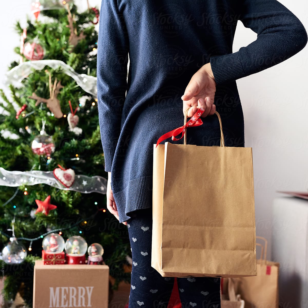 Kid holding present in paper bag Christmas tree.