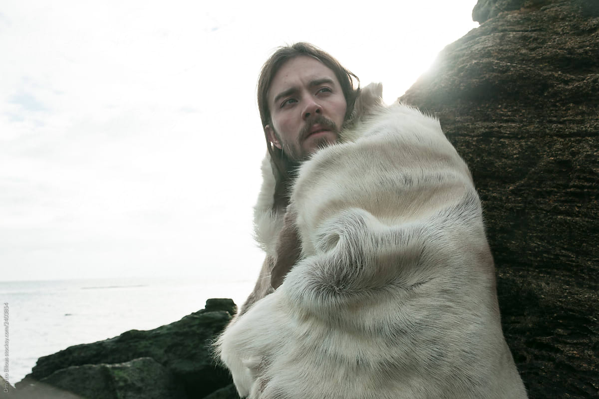 guy with long hair and a beard in the skin of an animal posing in the rocks