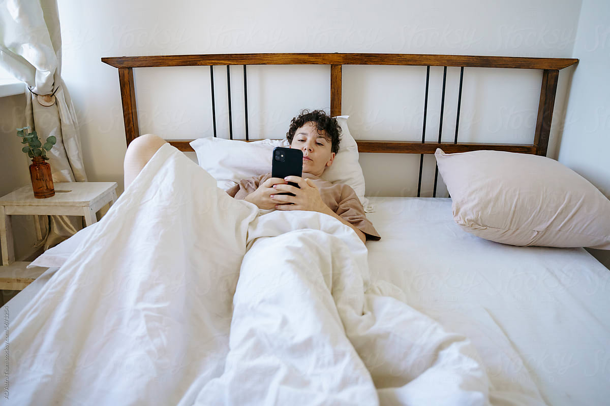 A woman has woken up and is holding a smartphone in her hands