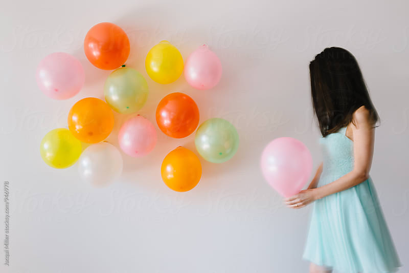 Woman holding pink balloon with more balloons  stuck on a white wall