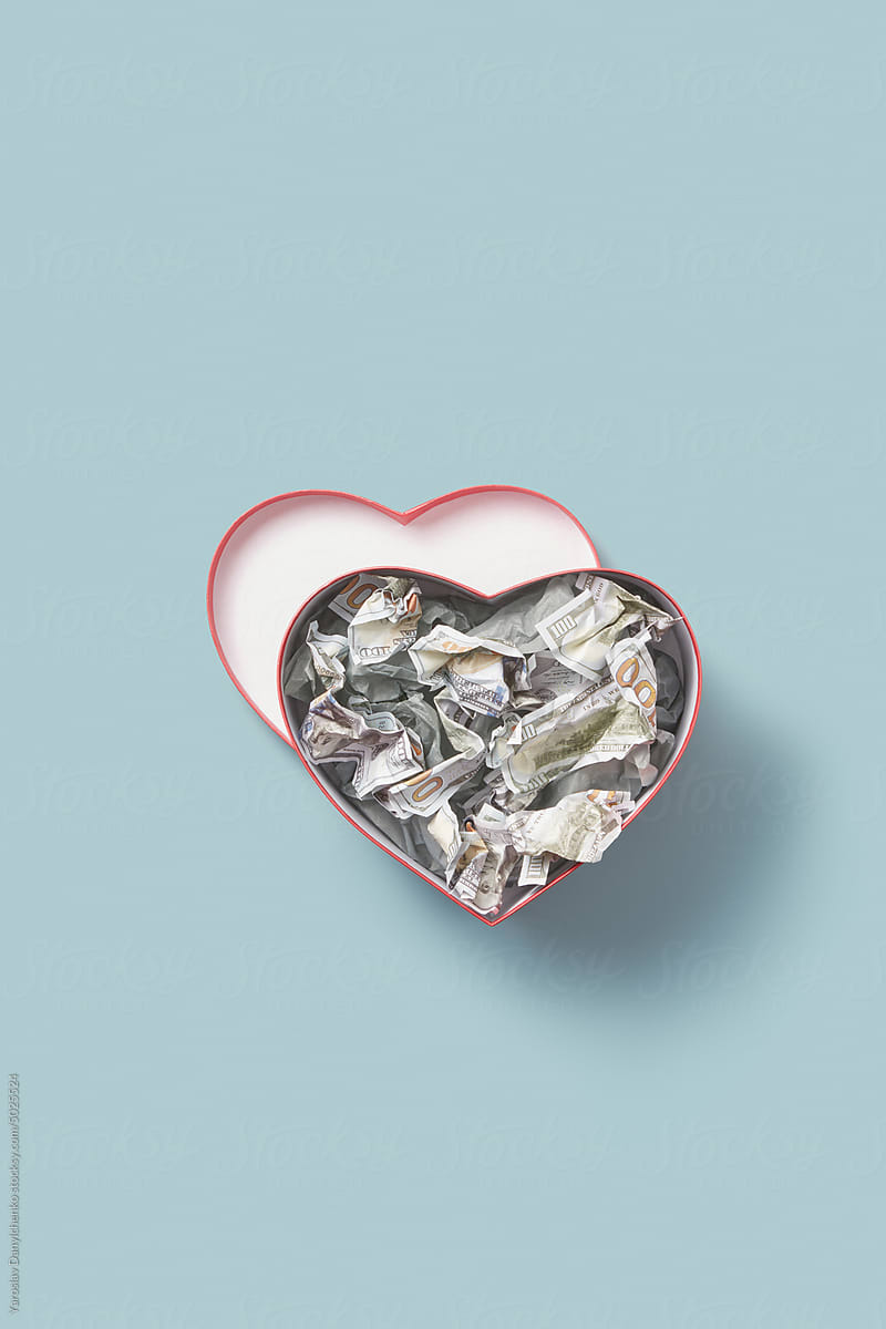 Crumpled dollar bills inside heart-shaped box.