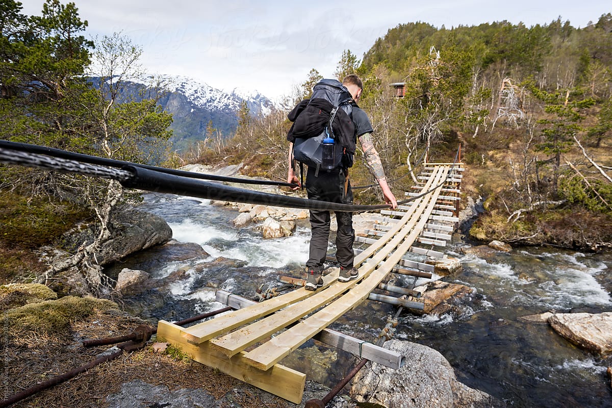 man crossing a river on a suspension bridge while hiking in Norway.
