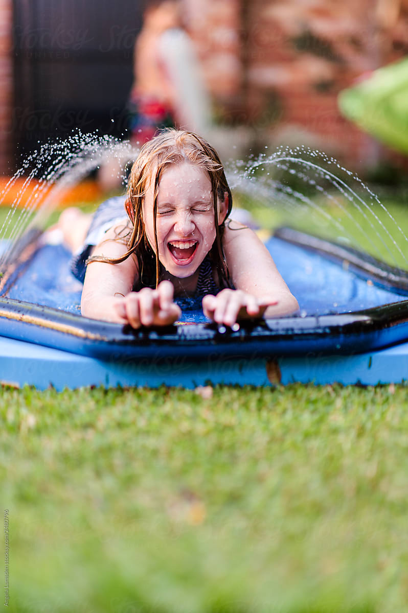 Girl having fun on a water spray slide mat in summer