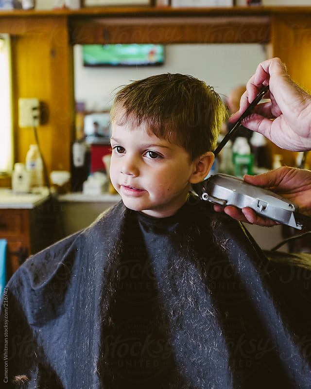 Handsome young boy getting his haircut in a barbershop by 