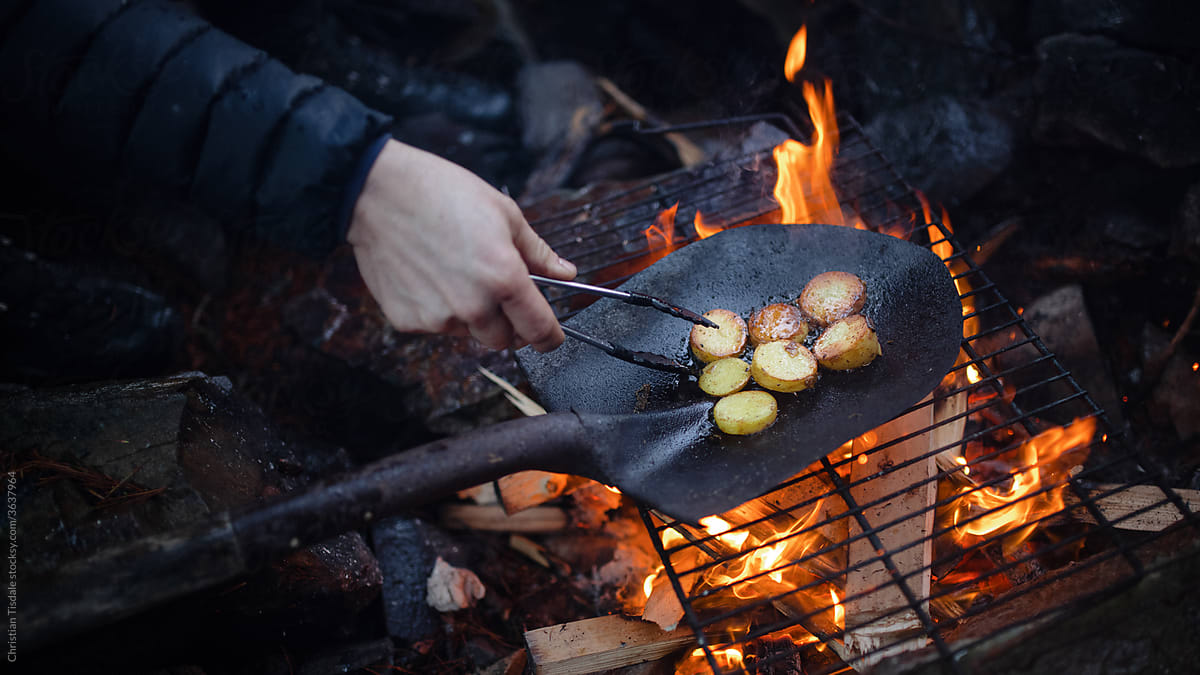 Potatoes being cooked over an open fire in a shovel