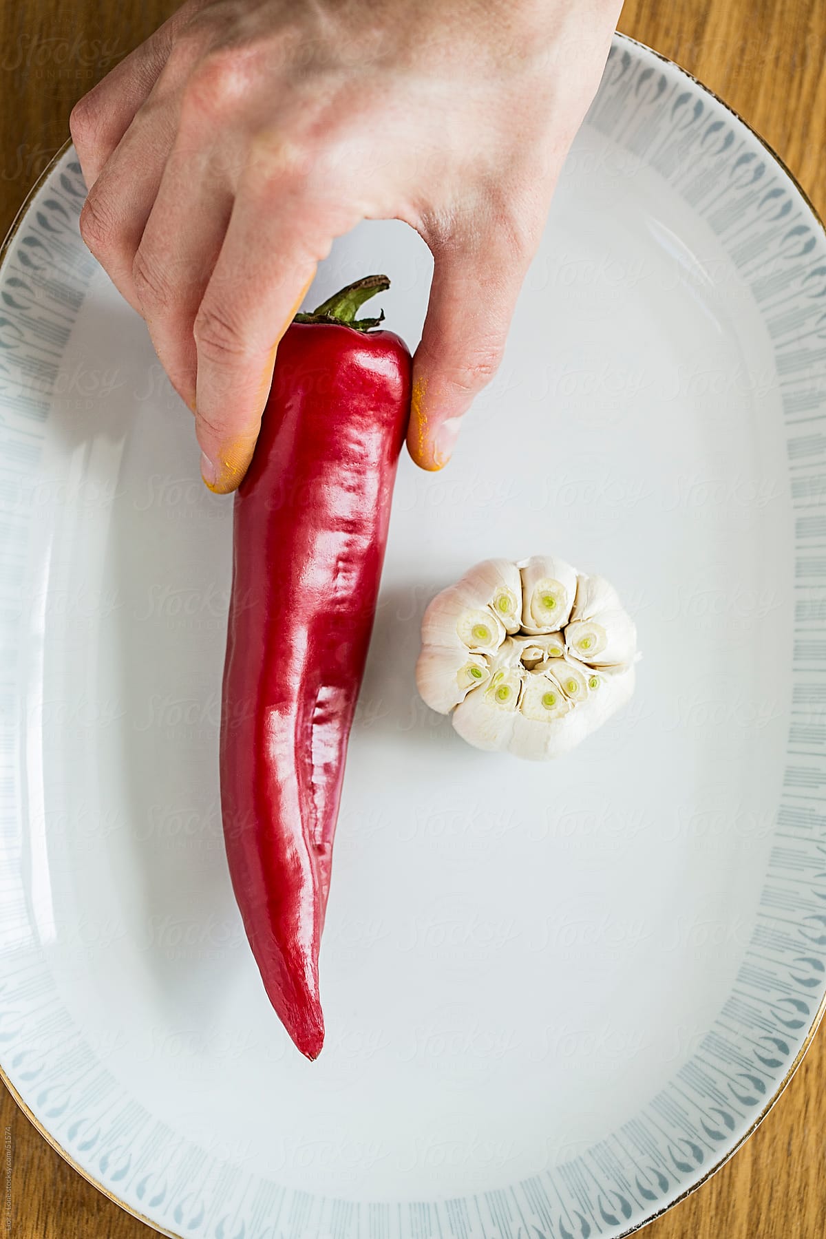 hand placing red pepper on vintage plate next to garlic