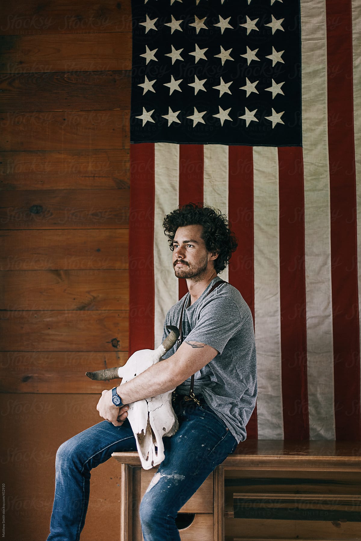 Portrait of a Confident Man Sitting in Front of an American Flag Holding a Bull Skull