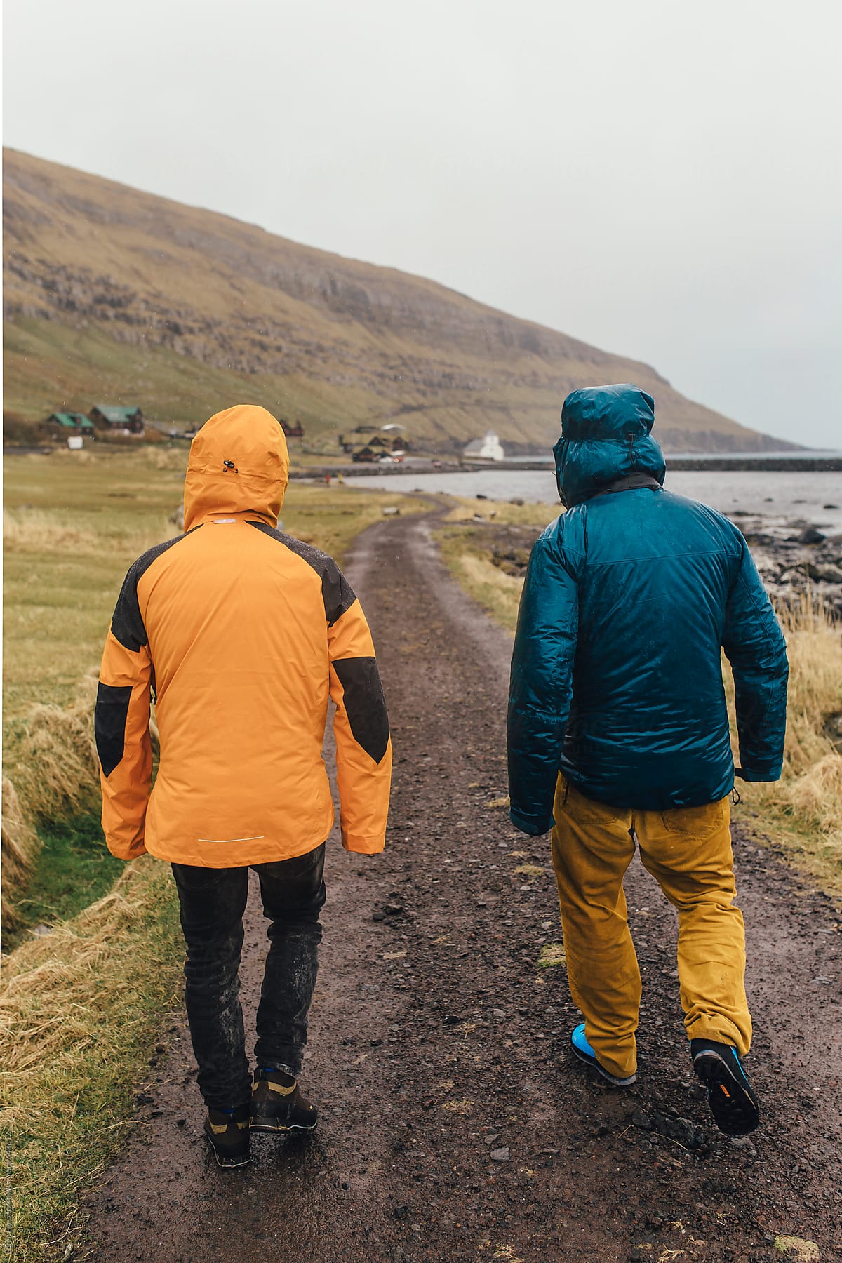 Two men walking in the rain by the sea.