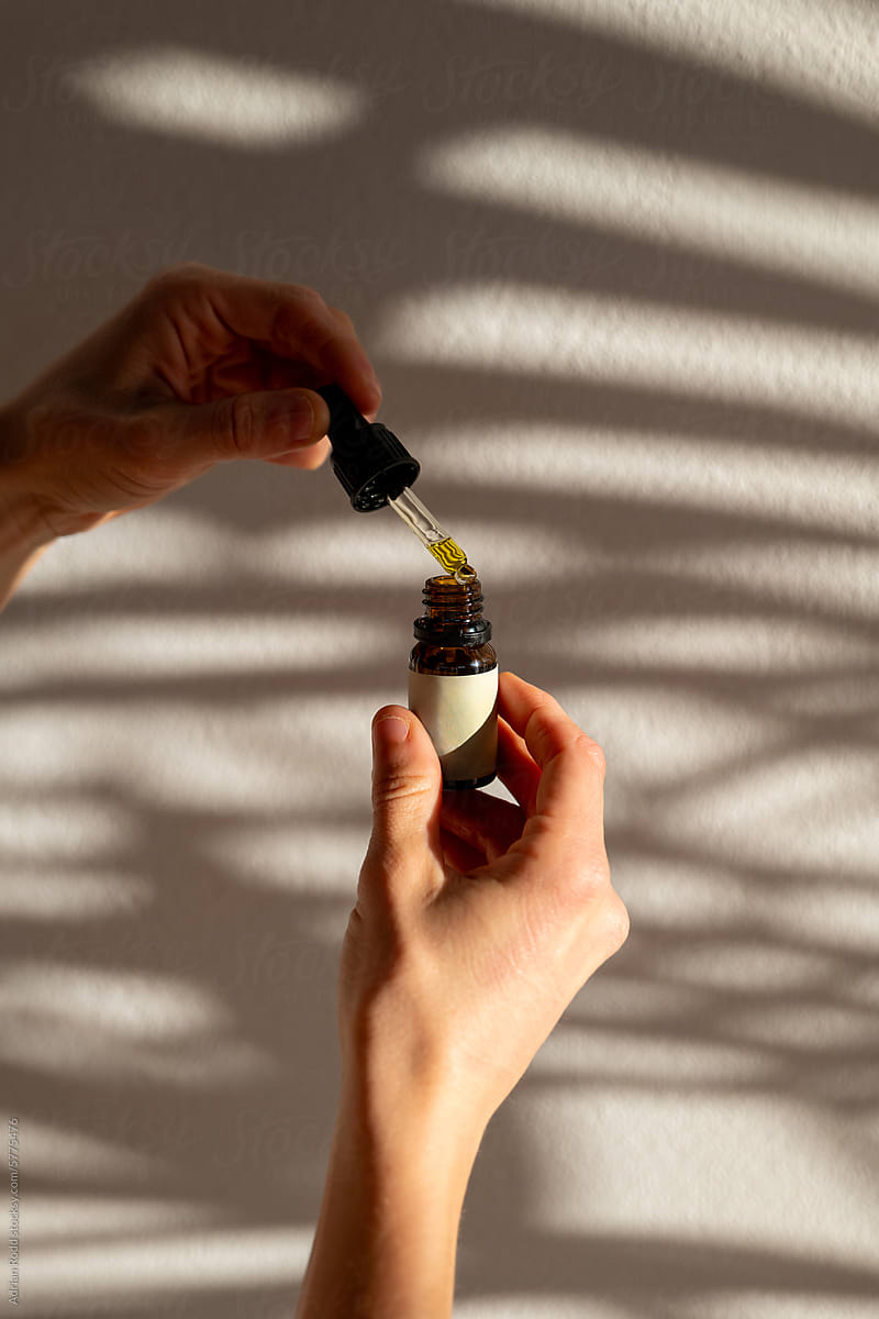 Close-up of the hands of a model holding a dropper with CBD oil
