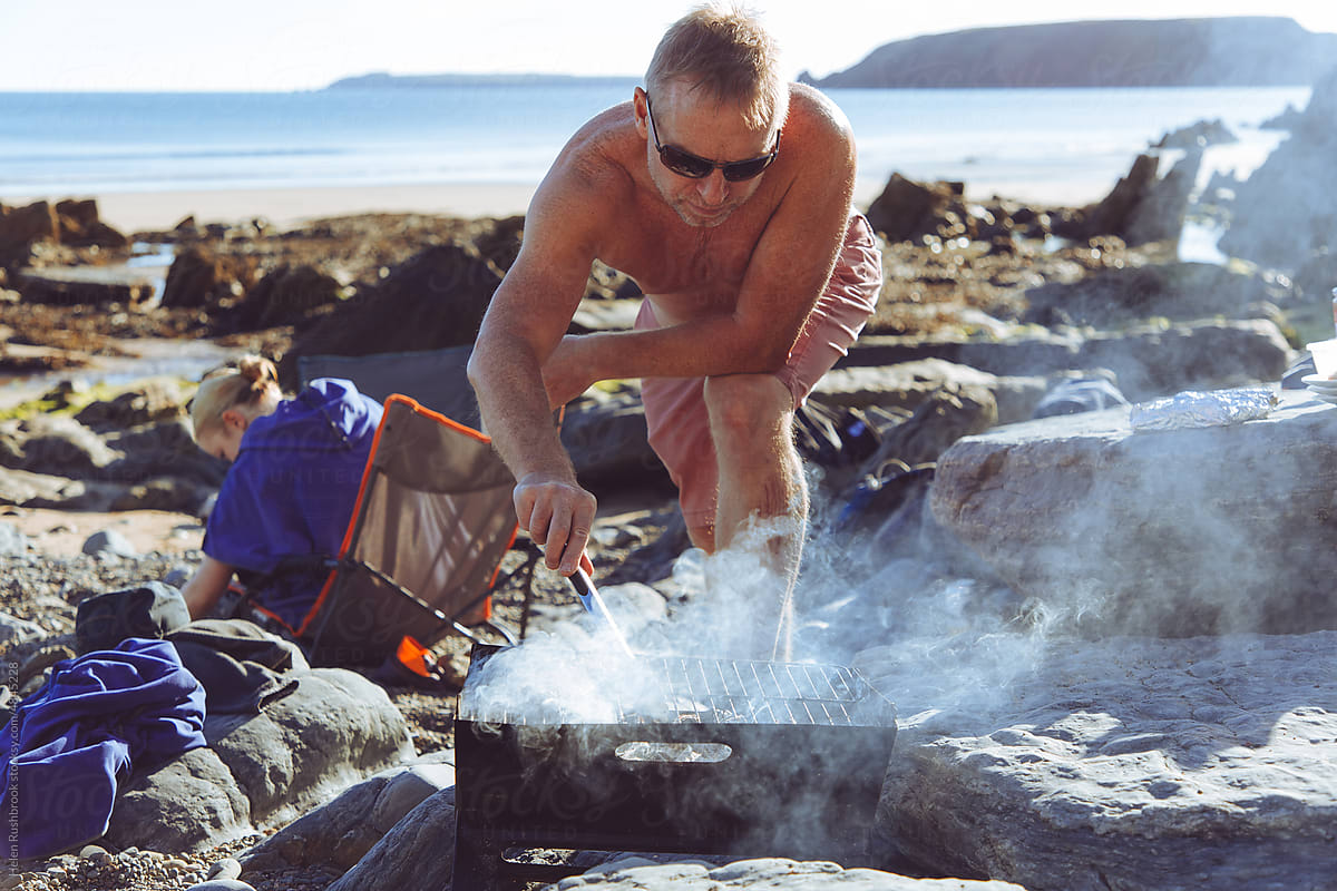 A man cooking burgers on a beach bbq