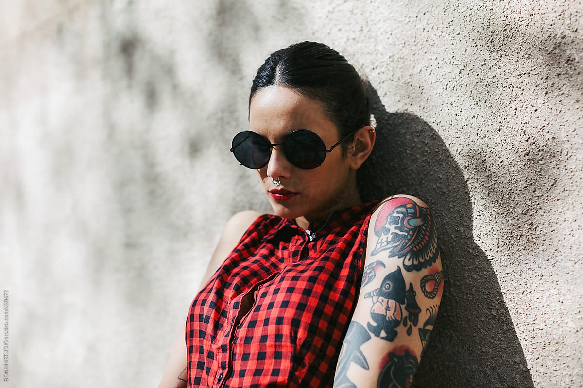 Portrait of an alternative woman with tattoos standing in front a wall.