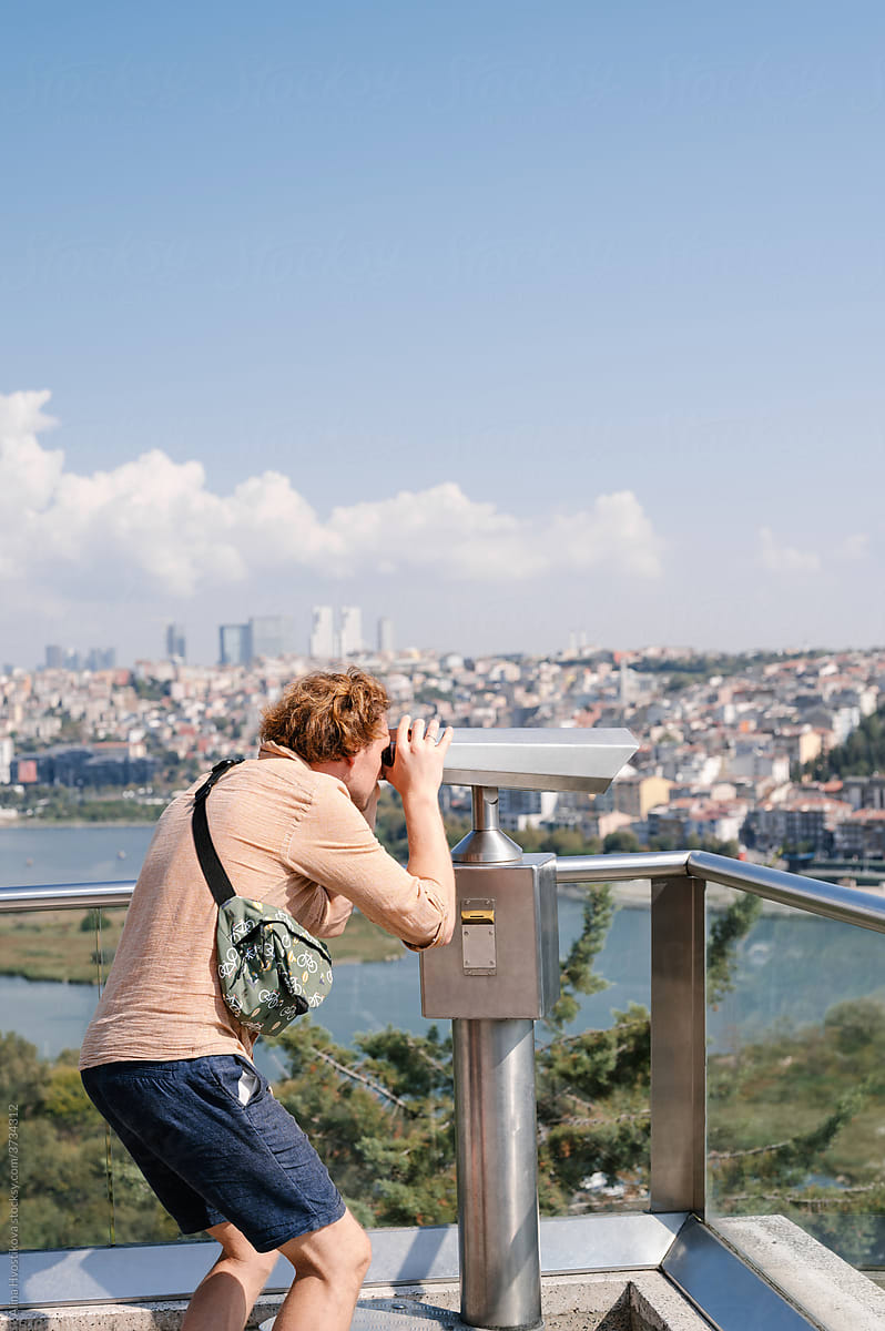 Male tourist admiring city through binoculars