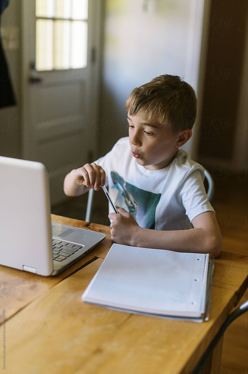 Little kid spending time online and using laptop at kitchen table