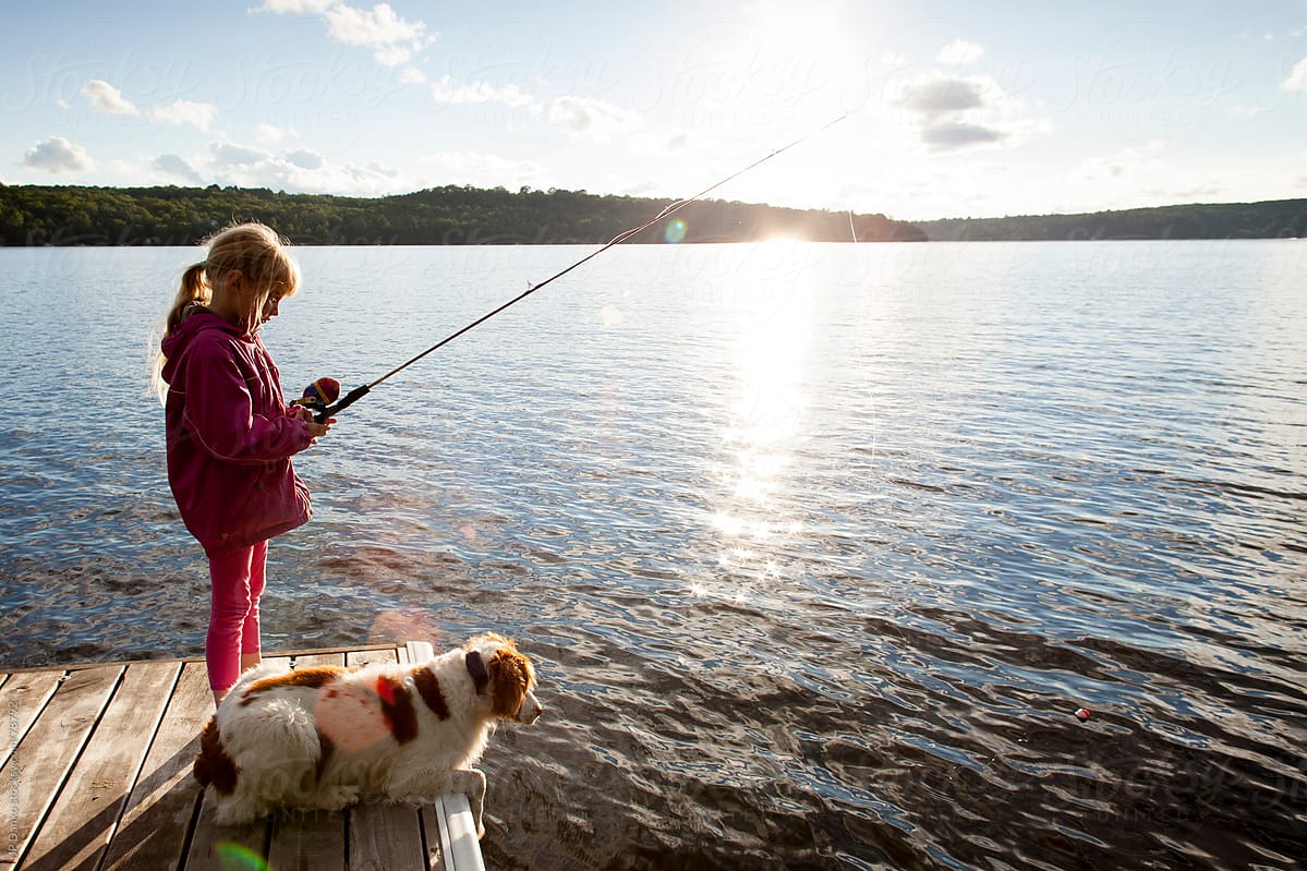 Little Girl Fishing From Dock On Cottage Lake With Dog by Stocksy