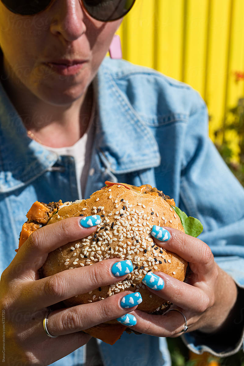 A woman with acrylic nails eating a burger