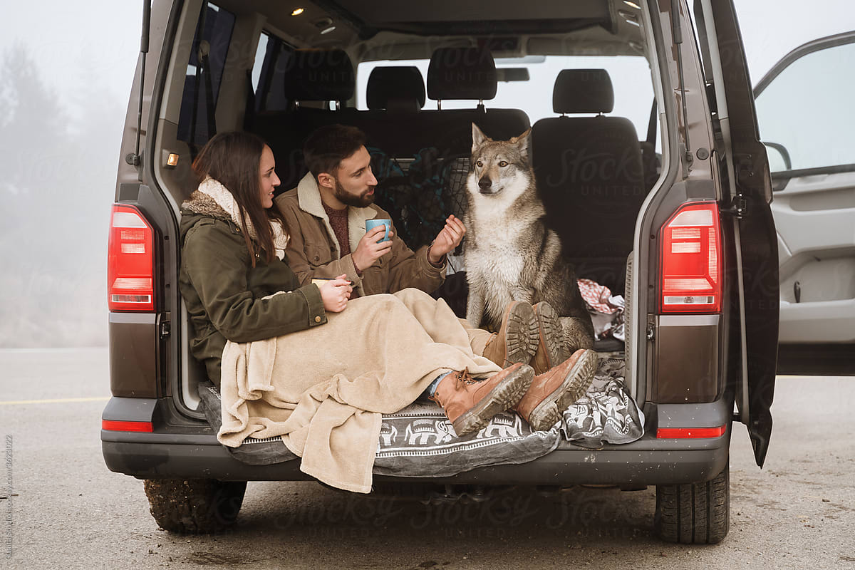 Young couple in a camper van in nature during winter having warm coffe with wolf dogs
