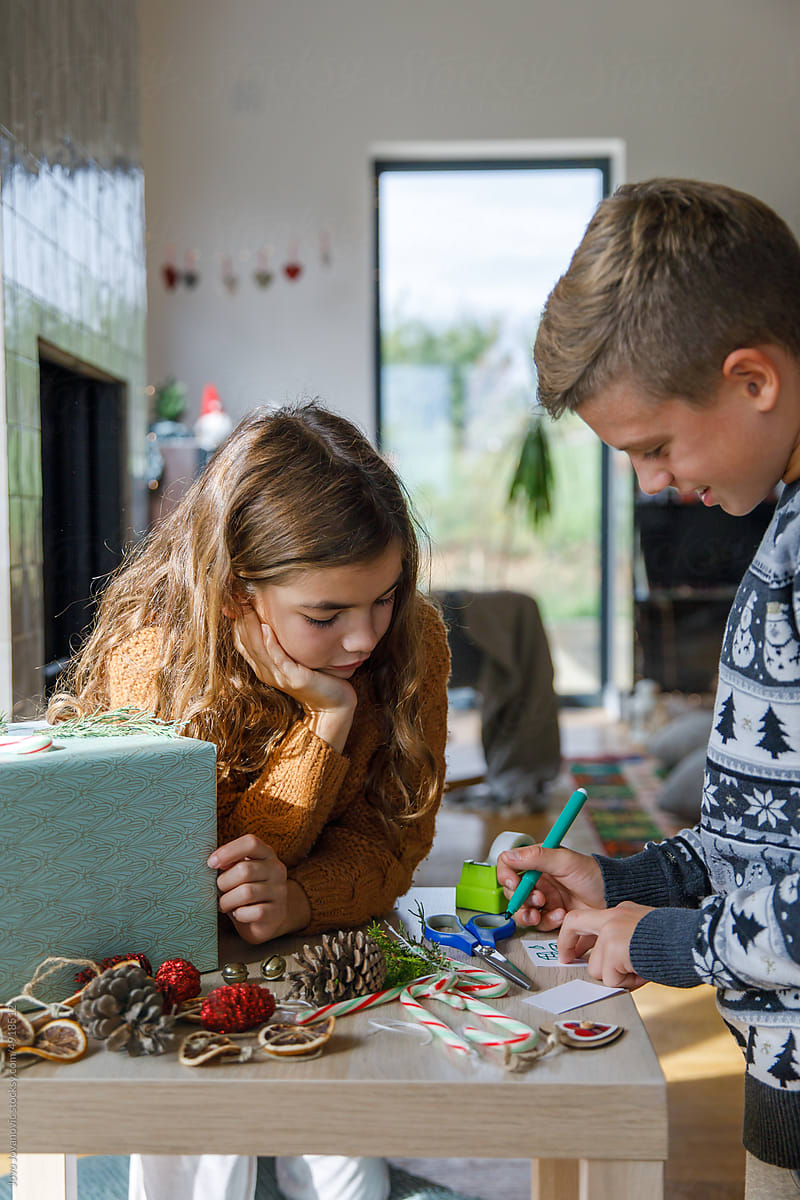 Siblings preparing decoration for Christmas gift at table