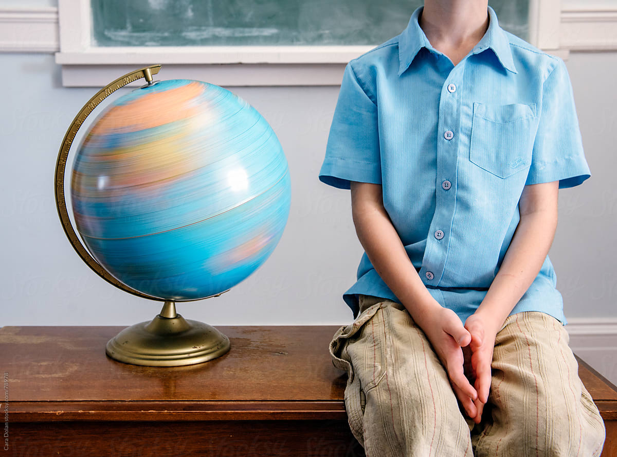 Student Sits Next to a Spinning Globe in a Classroom