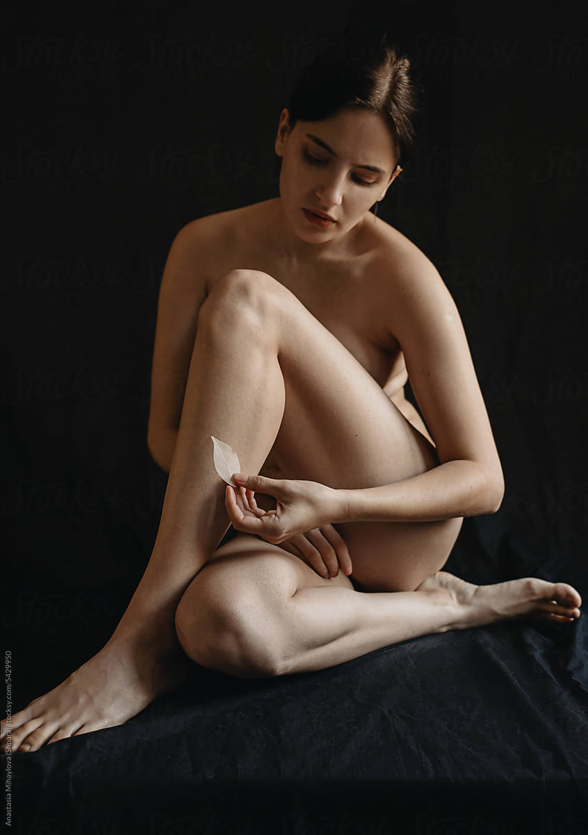 Sitting Nude Woman Holds In Hand A White Leaf With Her Fingers/