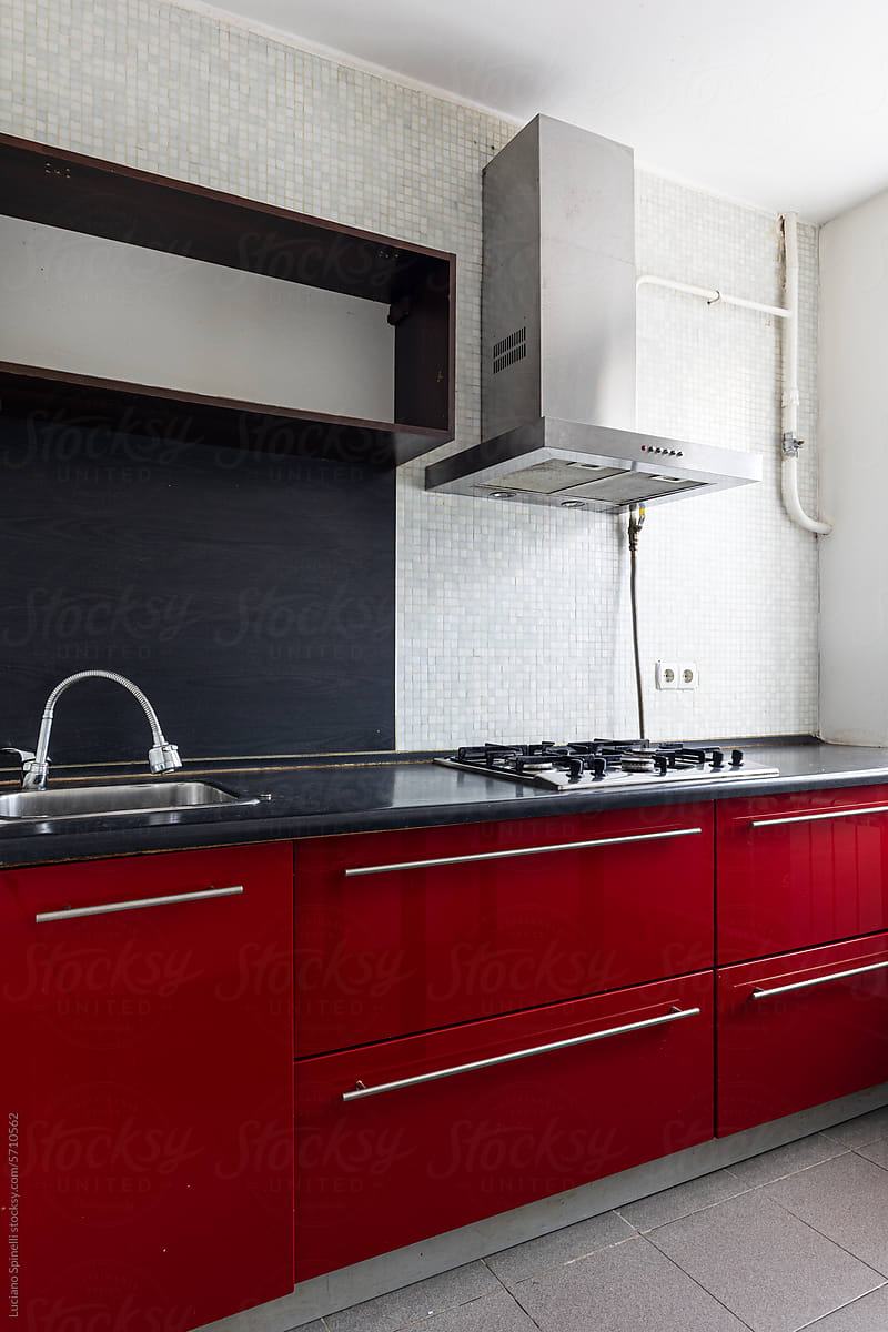 Kitchen cabinetry with red cabinet, black countertop and tiled wall