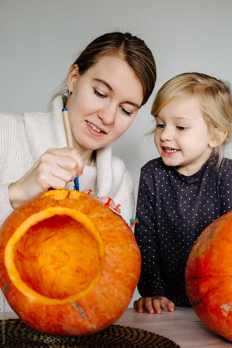 Woman with child making lantern from pumpkin