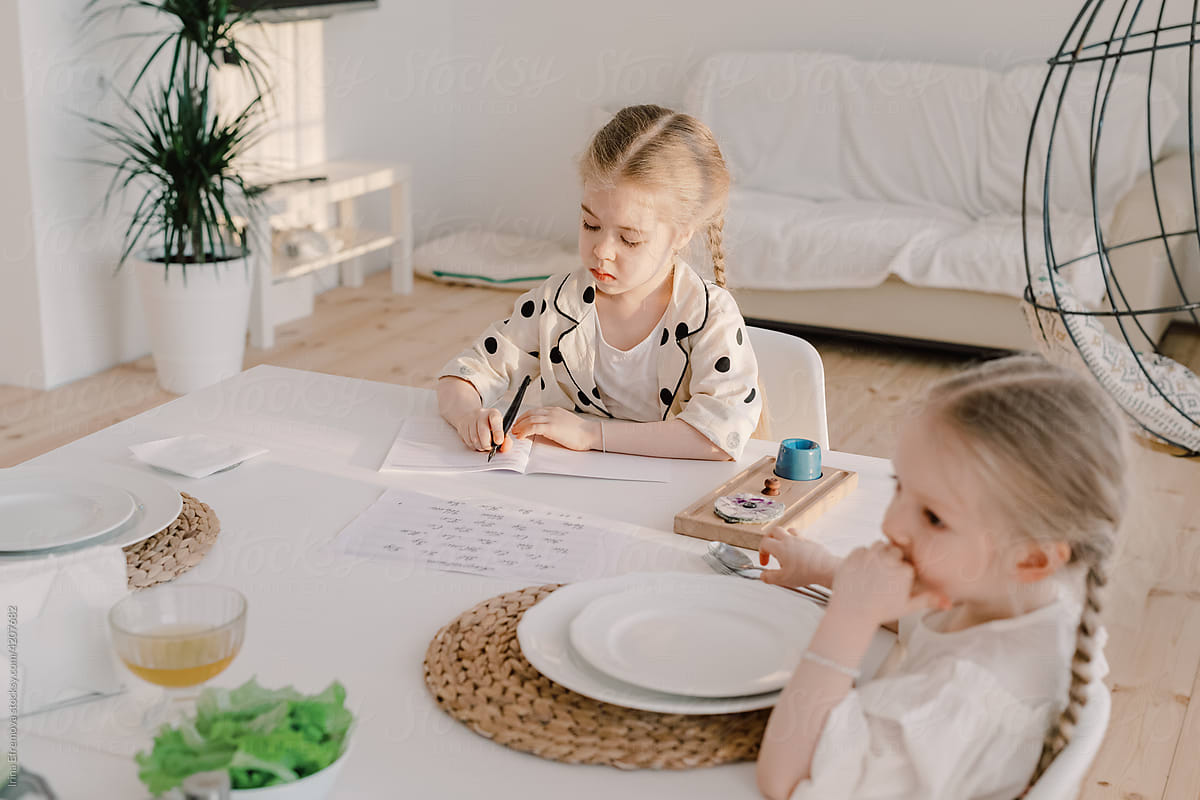 Girl doing homework at a dining table next to her little sister