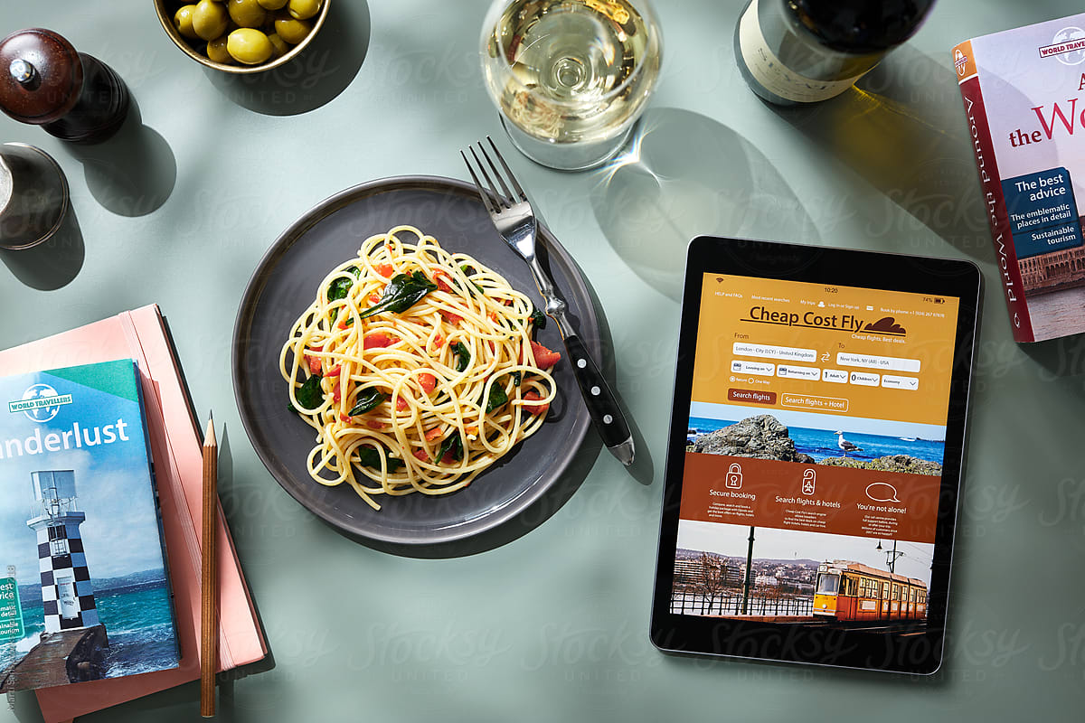 Digital tablet and pasta with travel books on table.