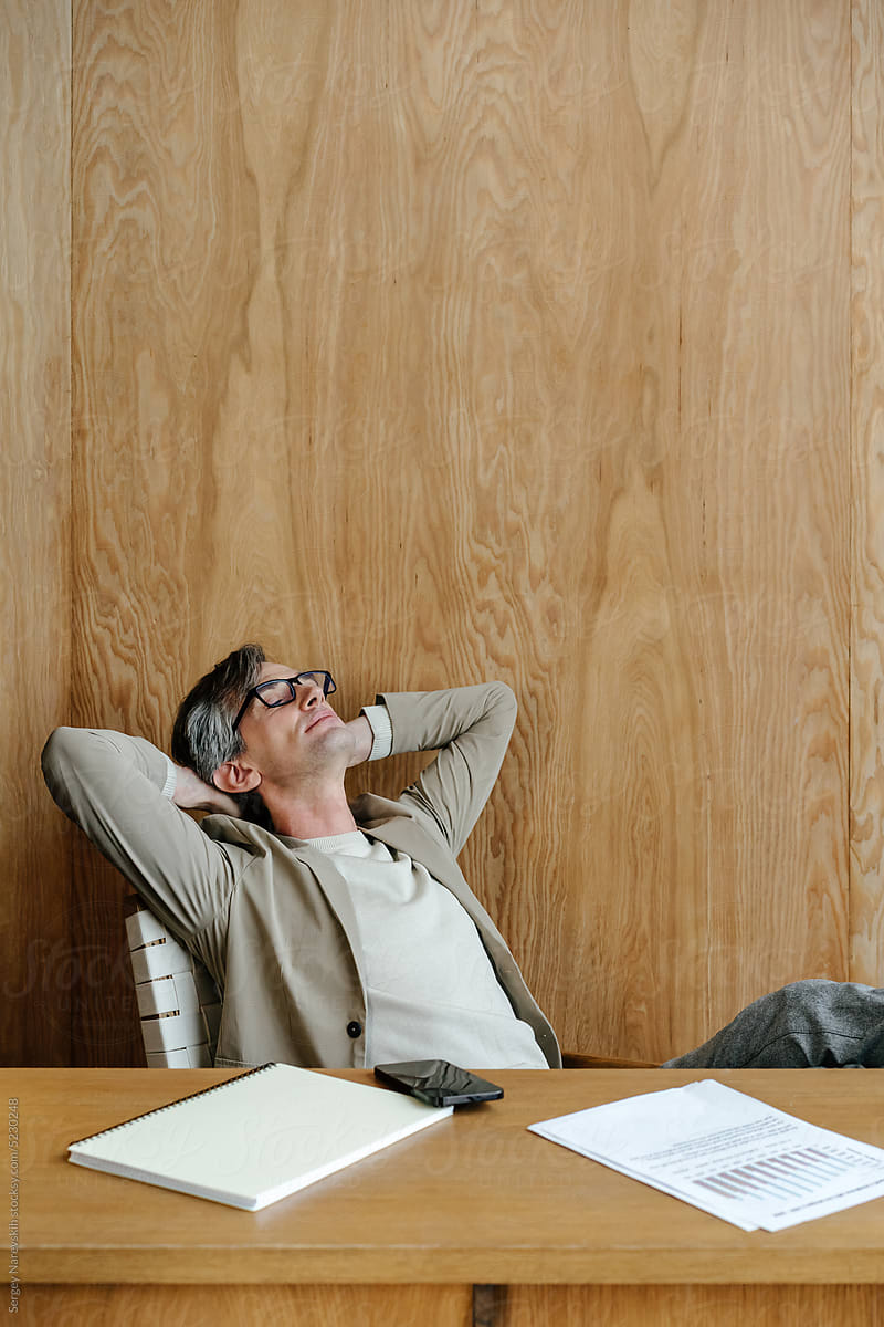 Mature male manager resting in workplace with hands behind head